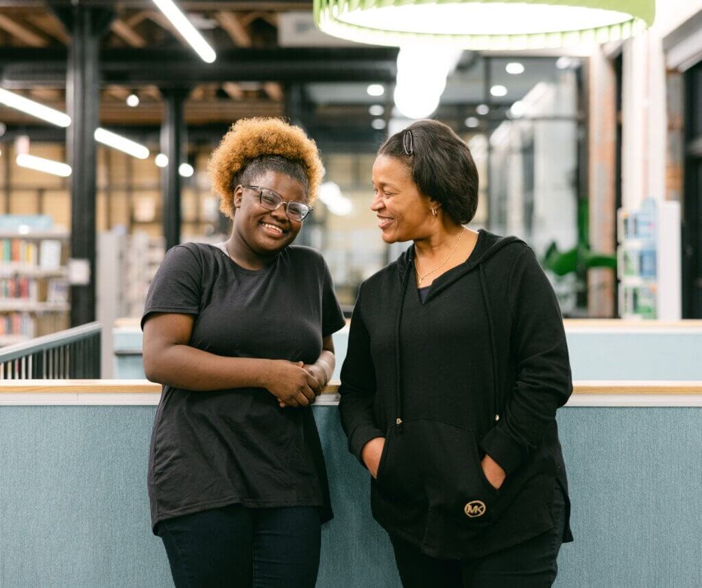 Black teenage girl laughs as older black woman looks at her smiling